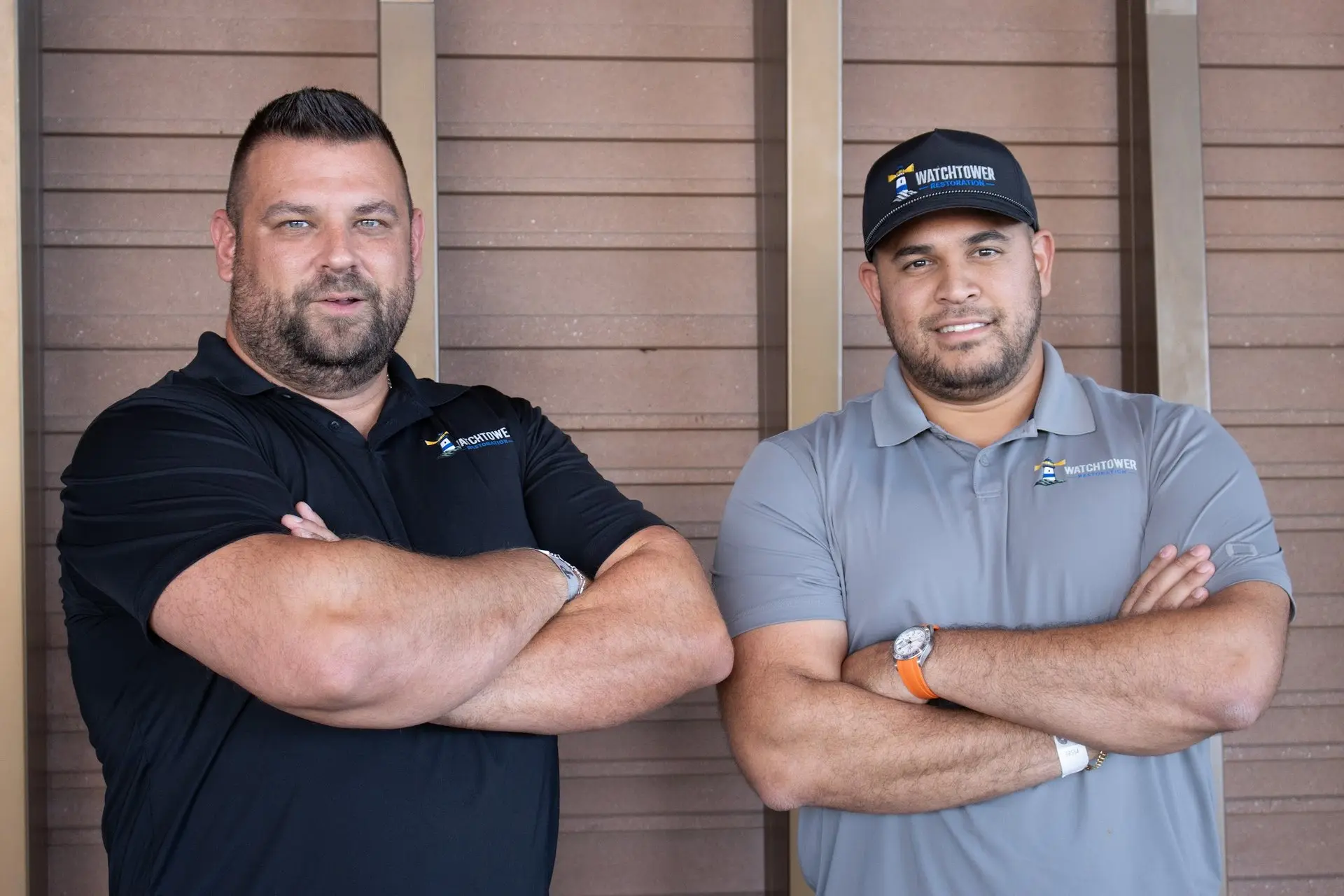 Two team members in polo shirts and a cap standing with arms crossed, water and fire damage restoration