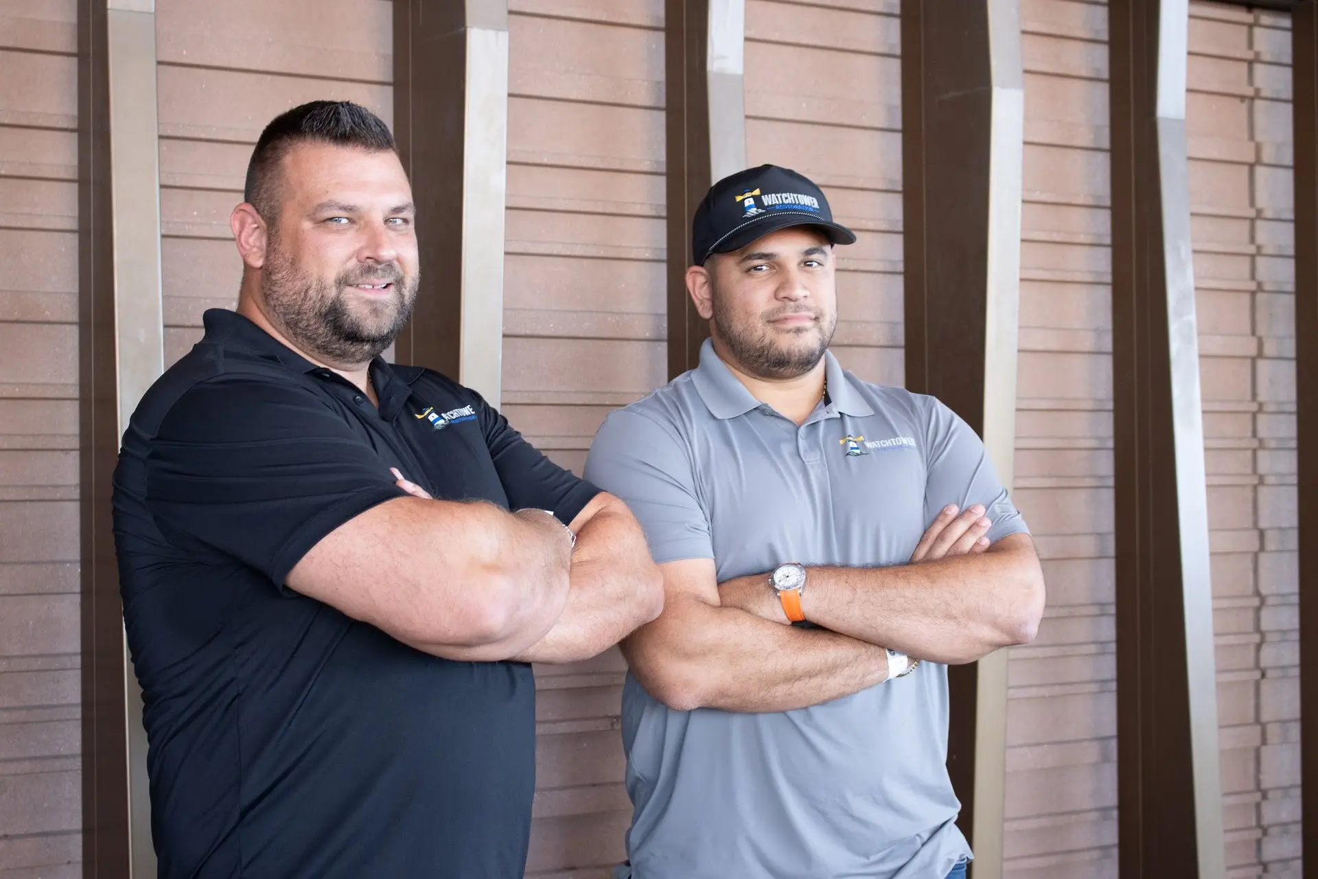 Two team members side by side, arms folded, in front of a slatted wall, water and fire damage restoration
