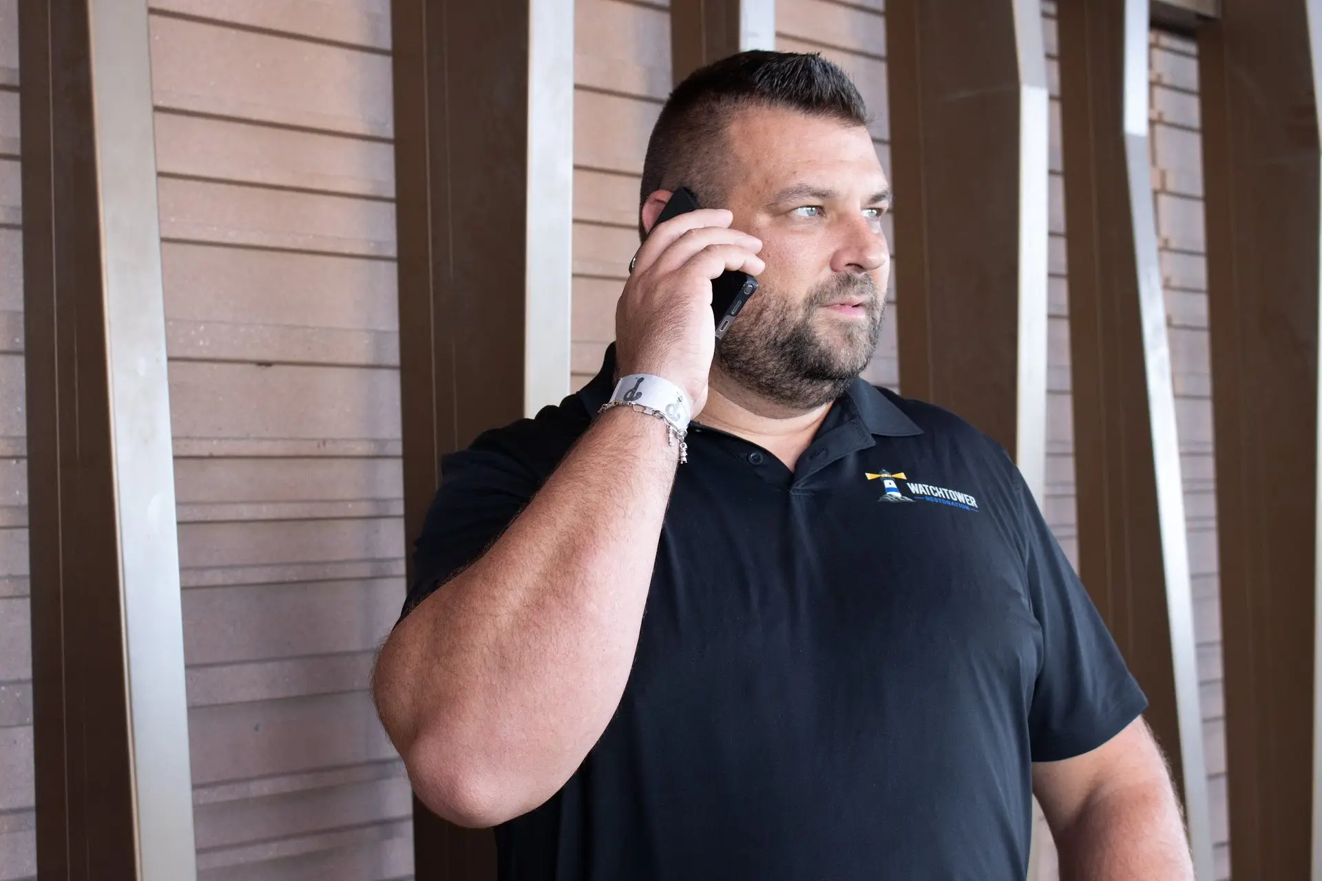 Team member in a black polo on a phone call beside a slatted wall, water and fire damage restoration