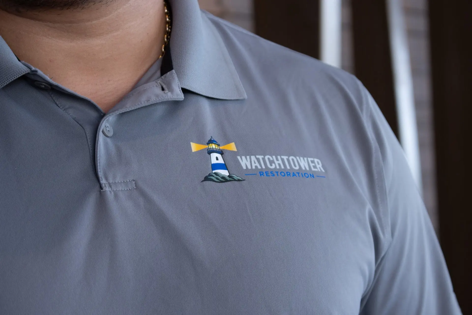 Close-up of the Watchtower Restoration logo on a grey polo shirt, water and fire damage restoration